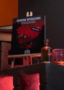 Shadow Operations book for Spire on cinder blocks with books, alcohol and smoke with red lighting © SHAW STUDIO