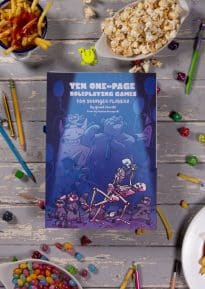 Front cover of Ten One-Page RPGs for Younger Players on a white table surrounded by dice, pencils and snacks © SHAW STUDIO